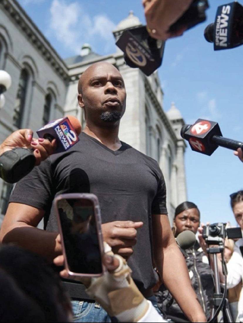 Valentino Dixon surrounded by reporters and news microphones outside a courthouse
